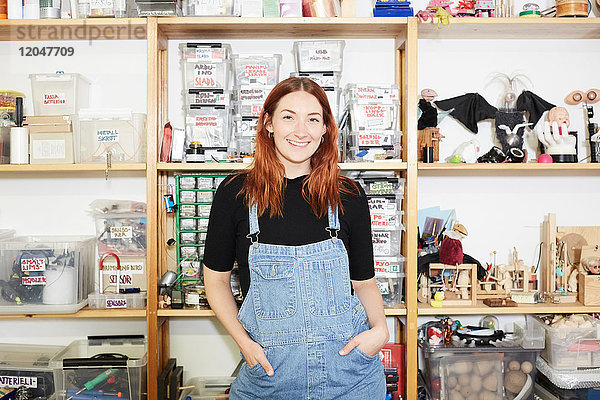 Porträt einer selbstbewussten rothaarigen Technikerin am Regal in der Werkstatt