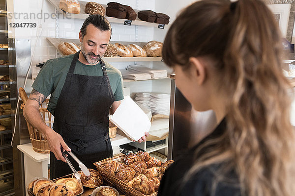 Lächelnder  reifer  männlicher Besitzer serviert der Kundin in der Bäckerei frisches Brot.