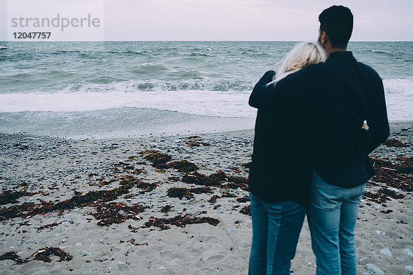 Rückansicht eines jungen Paares  das am Strand steht.