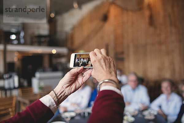 Abgeschnittenes Bild einer älteren Frau  die Freunde mit dem Smartphone im Restaurant fotografiert.