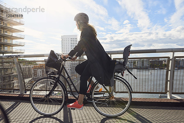 Seitenansicht der reifen Frau beim Radfahren auf der Fußgängerbrücke gegen den Himmel