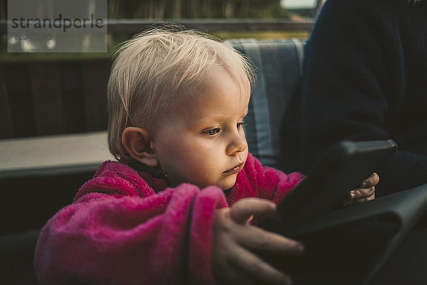 Nahaufnahme eines Mädchens  das ein digitales Tablett hält  während es von seiner Mutter sitzt.