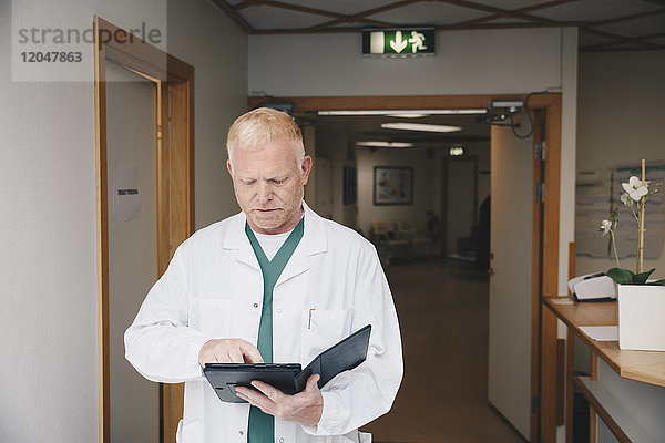 Reife Ärztin mit digitalem Tablett im Stehen im Krankenhausflur