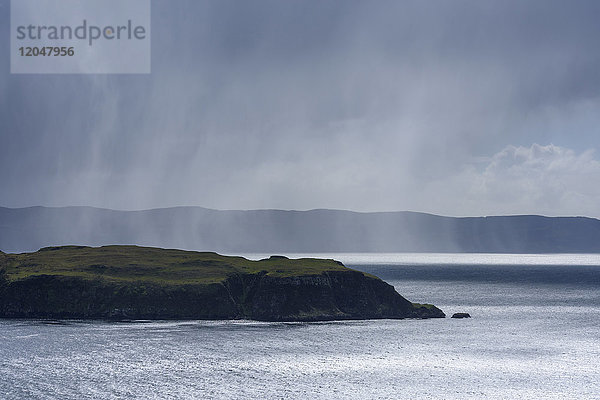 Sonnenbeschienene Meeresklippen und Regenwolken entlang der Küste der Isle of Skye in Schottland  Vereinigtes Königreich