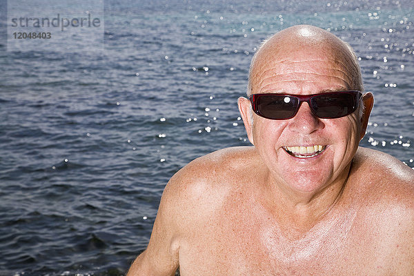 Porträt eines Mannes  der am See sitzt und eine Sonnenbrille trägt