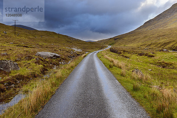 Kurvenreiche Straße in den Highlands mit bewölktem Himmel in Glen Coe in Schottland  Vereinigtes Königreich