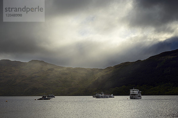Kreuzfahrtschiffe auf dem See mit dramatischen Wolken und Licht am Loch Lomond in Schottland  Vereinigtes Königreich