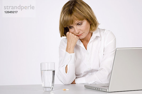 Frau mit Wasserglas  Pillen und Laptop-Computer