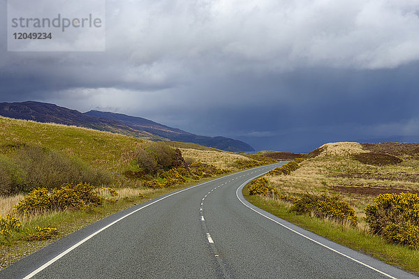 Kurvenreiche Landstraße mit Regenwolken im Frühling auf der Isle of Skye in Schottland  Vereinigtes Königreich