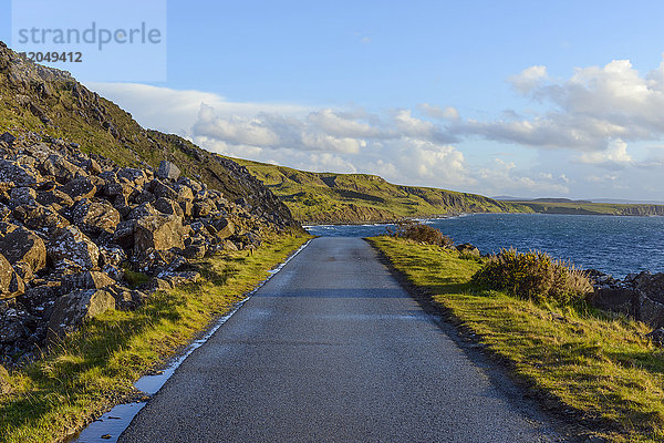 Typische schottische Landschaft auf der Isle of Sky mit einer Küstenstraße und Meeresklippen an einem sonnigen Tag in Schottland  Vereinigtes Königreich