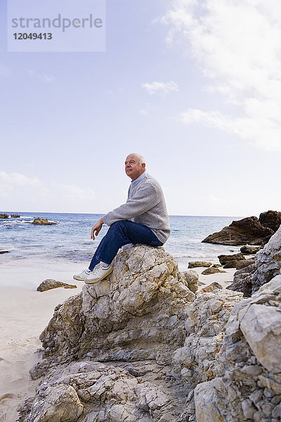 Mann auf Felsen am Strand sitzend