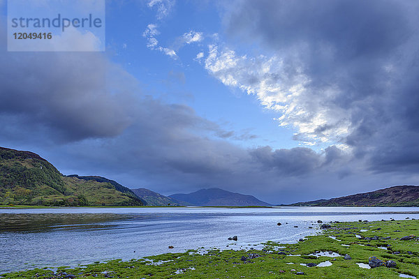 Grasbewachsene Küste mit dramatischen Wolken bei Sonnenaufgang entlang der schottischen Küste in der Nähe von Eilean Donan Castle und Kyle of Lochalsh in Schottland