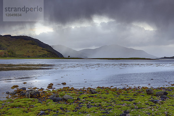 Regenwolken über dem grasbewachsenen Ufer entlang der schottischen Küste in der Nähe von Eilean Donan Castle und Kyle of Lochalsh in Schottland