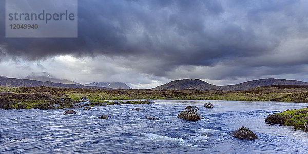 Fluss in Moorlandschaft mit dunklen Gewitterwolken und Bergen im Hintergrund im Rannoch Moor in Schottland  Vereinigtes Königreich