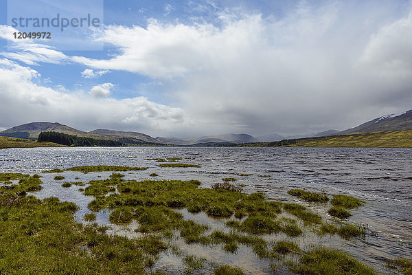 Grasbewachsenes Ufer und dramatische Wolkenformationen am Loch Tulla nahe Glen Coe in Schottland  Vereinigtes Königreich