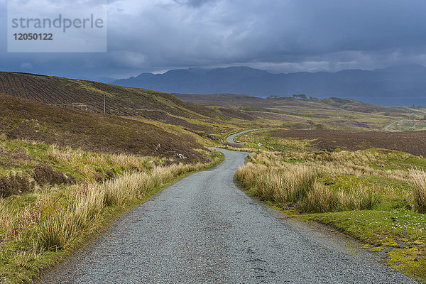 Kurvenreiche einspurige Straße durch die Landschaft bei bedecktem Himmel im Frühling auf der Isle of Skye in Schottland  Vereinigtes Königreich