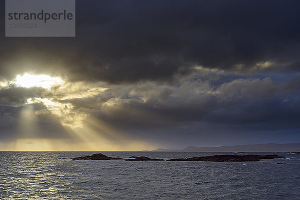 Die Sonne scheint durch die Sturmwolken bei Sonnenaufgang entlang der schottischen Küste bei Mallaig in Schottland  Vereinigtes Königreich