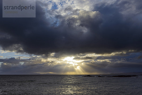 Die Sonne scheint durch die Sturmwolken bei Sonnenaufgang entlang der schottischen Küste bei Mallaig in Schottland  Vereinigtes Königreich