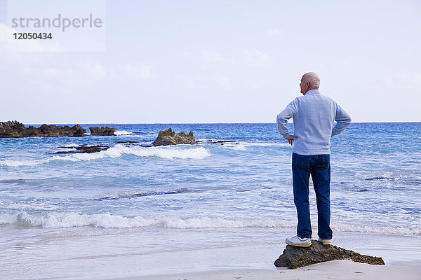 Mann steht auf einem Felsen und schaut aufs Meer hinaus