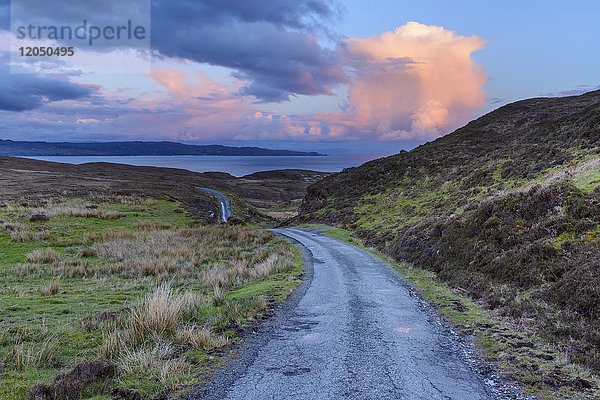 Alte kurvenreiche einspurige Straße im Frühling mit Kumulonimbuswolken bei Sonnenuntergang auf der Isle of Skye in Schottland  Vereinigtes Königreich