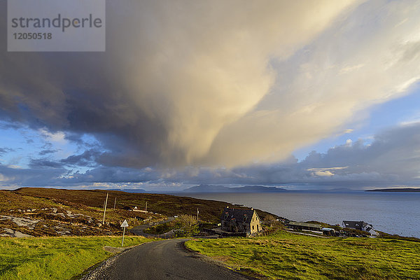 Straße  die zum Hafen führt  mit Häusern am Hang und Gewitterwolken über Loch Scavaig auf der Isle of Skye in Schottland