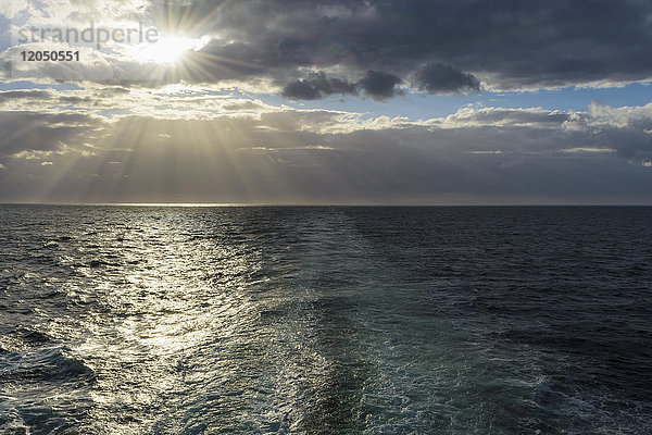 Kielwasser eines Schiffes mit Sonne  die durch die Wolken über der Nordsee scheint  Vereinigtes Königreich