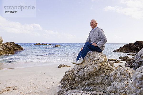Mann auf Felsen am Strand sitzend