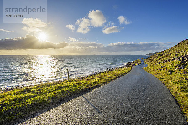 Typische schottische Landschaft auf der Isle of Skye mit einer Küstenstraße und der Sonne  die über dem Meer scheint  Schottland  Vereinigtes Königreich