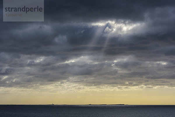 Die Sonne scheint durch Regenwolken über der Farne-Insel in der Nordsee bei Bamburgh  England  Northumberland