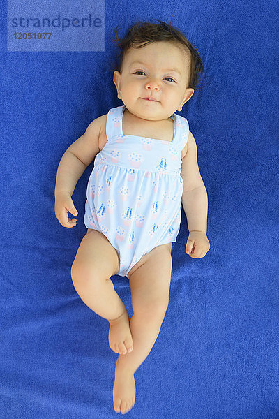 Ein Jahr altes Mädchen im Badeanzug auf einem blauen Strandtuch liegend