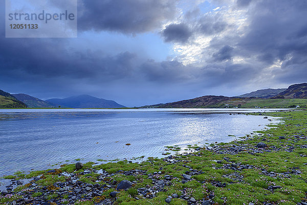 Grasbewachsene Küste mit dramatischen Wolken bei Sonnenaufgang entlang der schottischen Küste in der Nähe von Eilean Donan Castle und Kyle of Lochalsh in Schottland