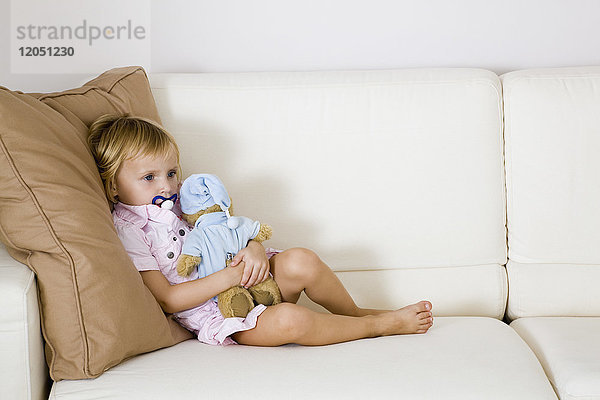 Kleines Mädchen sitzt auf dem Sofa und hält ein Kuscheltier