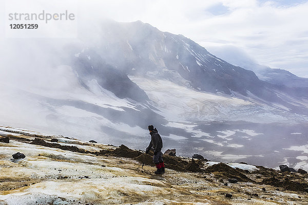 Ein Mann blickt durch die Wolken auf den Trident Volcano  während er die Knife Creek Gletscher im Katmai National Park besteigt; Alaska  Vereinigte Staaten von Amerika