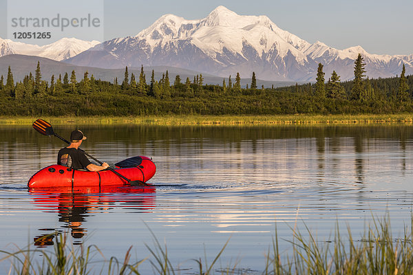 Ein Mann paddelt auf einem Packfloß über den Donnelly Lake mit dem in der Ferne aufragenden Mt. Hayes; Alaska  Vereinigte Staaten von Amerika