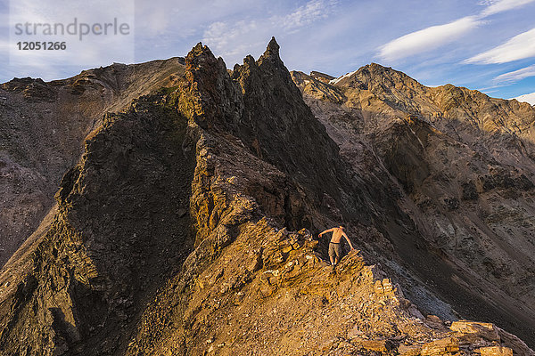 Ein Wanderer ohne Hemd klettert im Sommer über einen zerklüfteten Bergrücken in der östlichen Alaska Range in der Nähe des Whistler Creek; Alaska  Vereinigte Staaten von Amerika