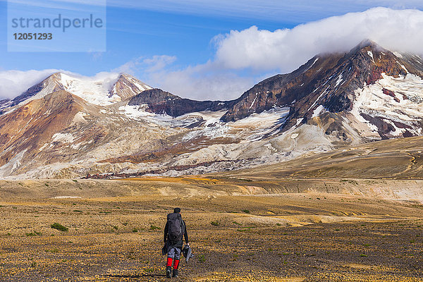 Ein Rucksacktourist durchquert die exotische Landschaft des mit Asche und Bimsstein bedeckten Valley of Ten Thousand Smokes im Katmai National Park  mit dem Mt. Katmai (links)  dem Trident Volcano (rechts) und den Knife Creek Gletschern in der Ferne; Alaska  Vereinigte Staaten von Amerika