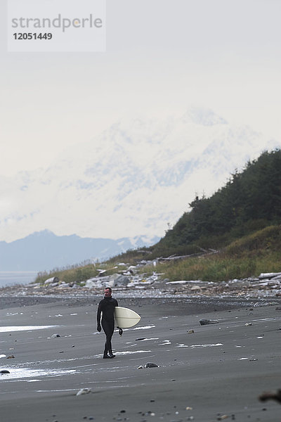 Surfer hält Surfbrett und geht am Ufer in der Nähe von Yakutat  Südost-Alaska  USA