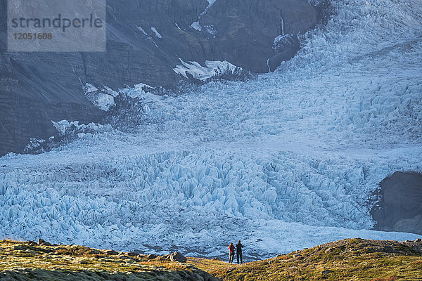 Ein Paar  das vor einem Gletscher an der Südküste Islands steht und die Natur von ihrer besten Seite bewundert; Island