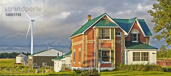 Ein Bauernhaus mit einer Scheune  einem Silo und einer Windturbine dahinter und weidendem Vieh auf einem Feld; Flesherton  Ontario  Kanada