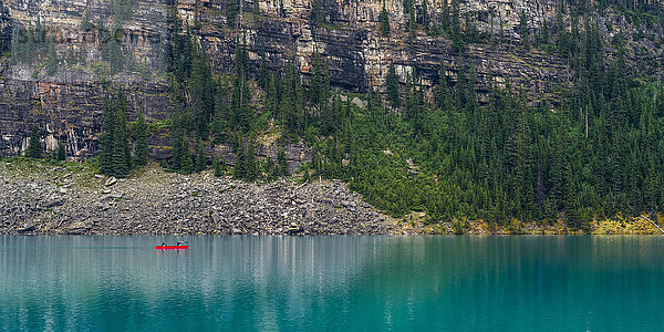 Ein rotes Kanu im Moraine Lake mit einer Klippe der kanadischen Rocky Mountains entlang der Uferlinie; Lake Louise  Alberta  Kanada