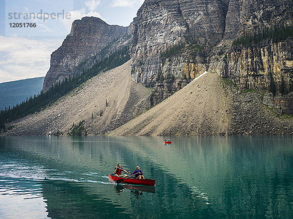 Ein rotes Kanu im Moraine Lake mit einer Klippe der kanadischen Rocky Mountains entlang der Uferlinie; Lake Louise  Alberta  Kanada