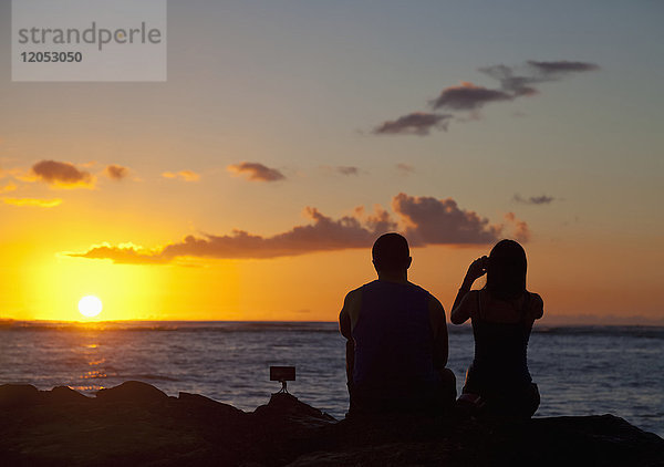 Silhouette eines Paares  das Fotos macht und den Sonnenuntergang am Strand beobachtet  Waikiki; Honolulu  Oahu  Hawaii  Vereinigte Staaten von Amerika