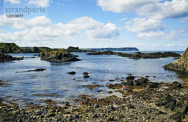 Zerklüftete Küste Nordirlands mit einem kleinen Mädchen  das mit einem Netz auf den Felsen am Rande des Wassers sitzt; Irland