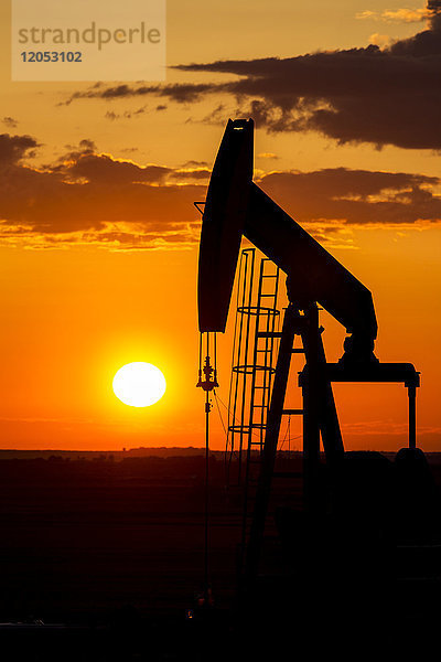 Silhouette eines Pump Jack bei Sonnenaufgang mit einer bunten Orange Sonne  Wolken und Himmel; Alberta  Kanada