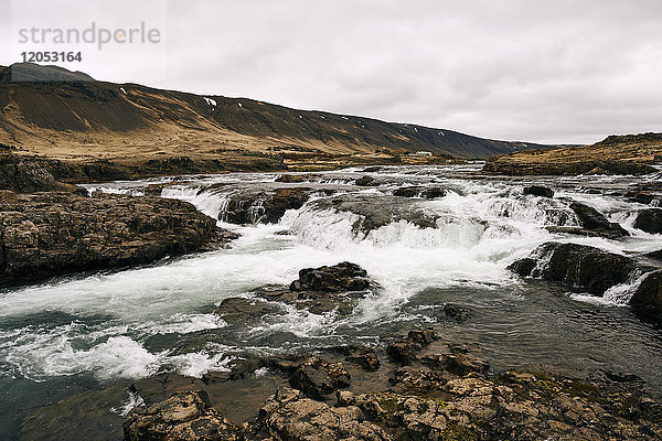 Wasser fließt über Felsen in einer Landschaft unter einem bewölkten Himmel; Island