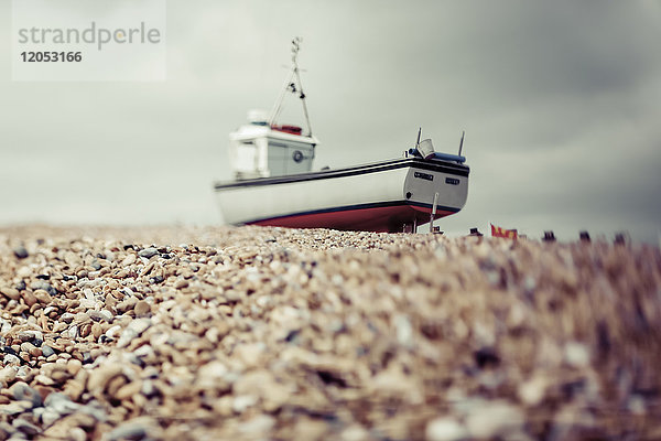 Ein Fischerboot liegt am felsigen Strand unter einem bewölkten Himmel; Hastings  England