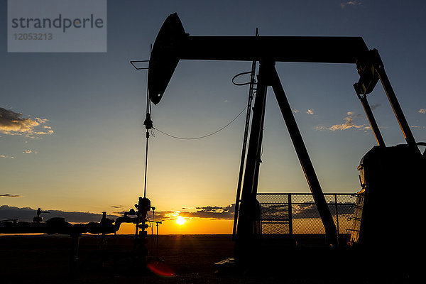 Silhouette eines Pumpjack und gut Kopf bei Sonnenaufgang mit einem bunten Orange Sonne  Wolken und Himmel; Alberta  Kanada