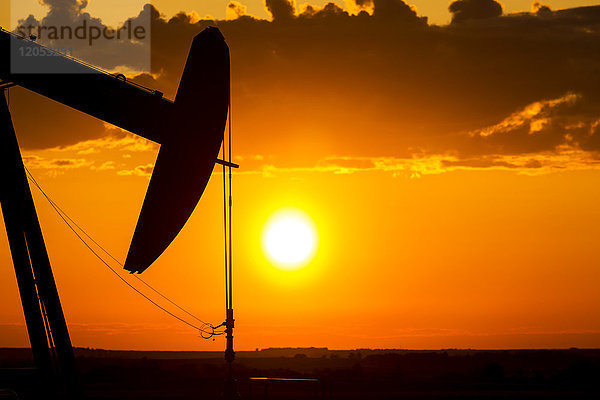 Silhouette eines Pumpjack Kopf bei Sonnenaufgang mit einem bunten Orange Sonne  Wolken und Himmel; Alberta  Kanada