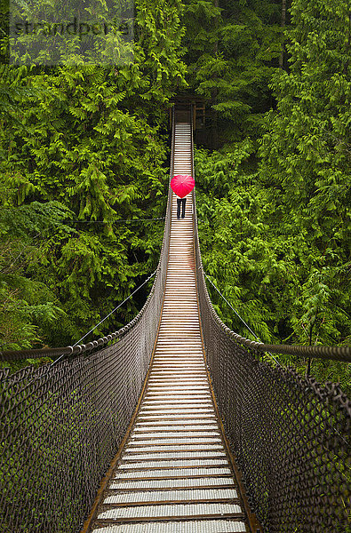 Frau mit einem roten  herzförmigen Regenschirm beim Überqueren der Lynn-Canyon-Hängebrücke  Nord-Vancouver; Vancouver  British Columbia  Kanada