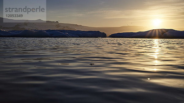 Goldener Sonnenuntergang über den Silhouetten der Berge entlang der ruhigen Wasser- und Küstenlinie; Island